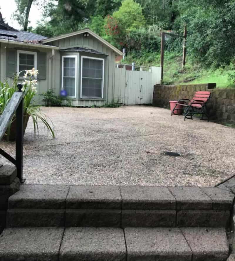 Exposed-aggregate front patio and block steps after washing, in front of a gray cottage with a bay window and a red glider bench