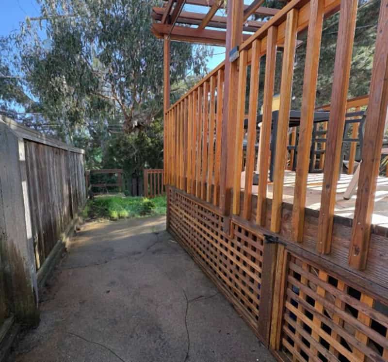 Redwood deck with lattice skirting and a pergola next to a concrete side walkway