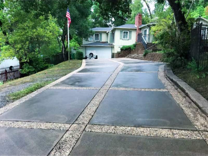 Exposed-aggregate driveway after pressure washing, even gray panels and clean pebble bands running up to a two-story house