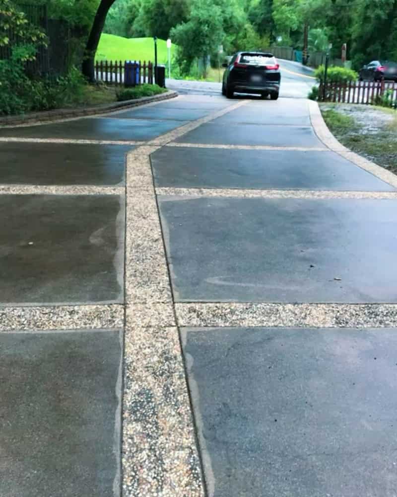 Exposed-aggregate driveway just after washing, still wet, seen from the top looking down to the street, with our lettered SUV parked at the bottom