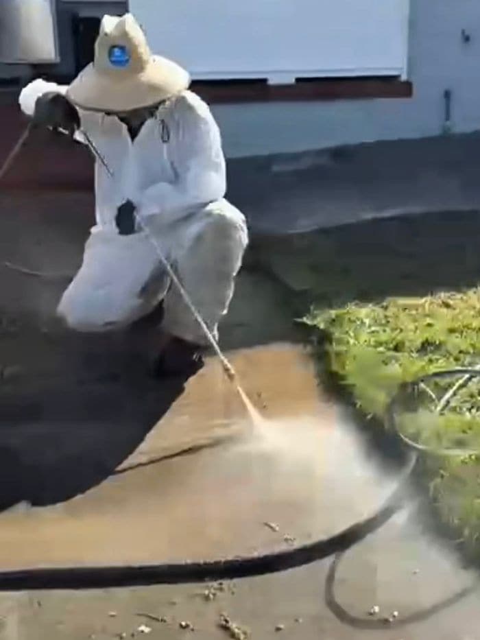 Technician crouched and pressure washing a concrete slab, with a clean strip beside darker dirty concrete
