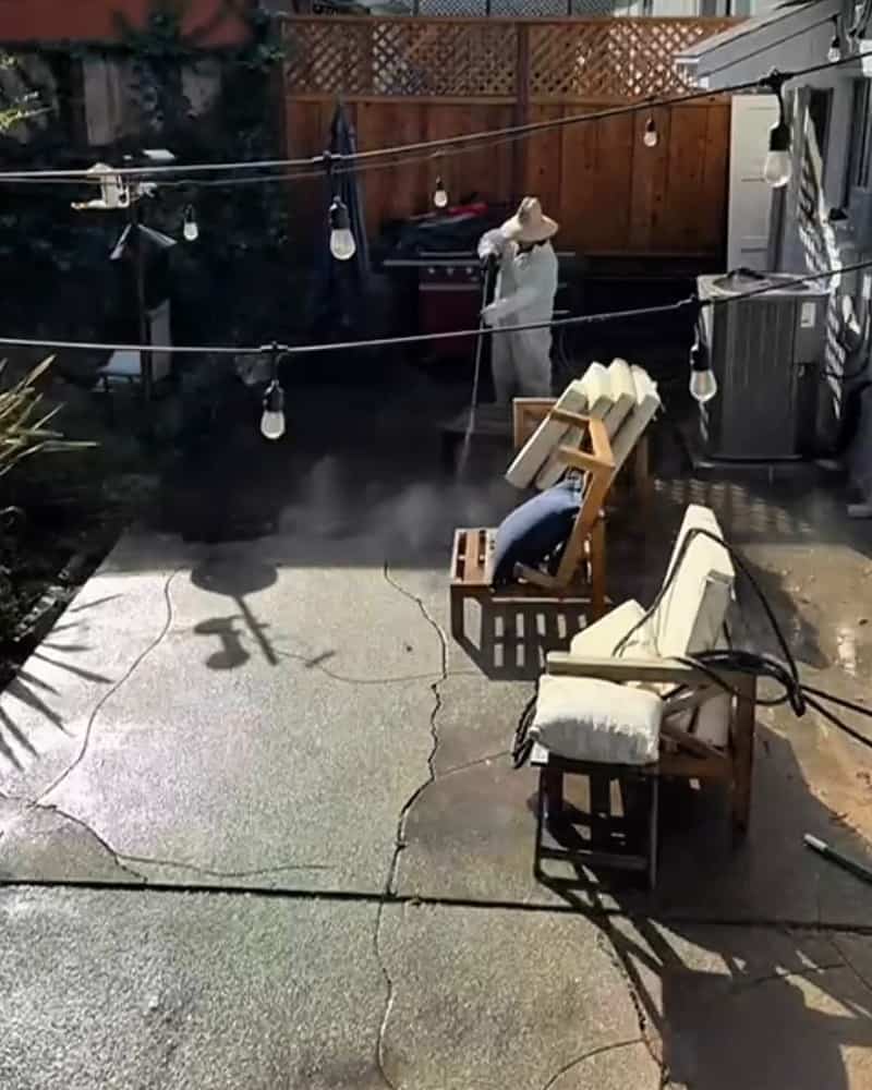 The same backyard patio partway through washing, clean gray concrete in front and dirty concrete at the far end