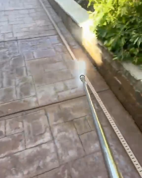 Pressure washer wand over a stamped concrete side path beside a block planter wall