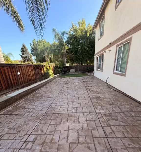 Stamped concrete patio running along the side of a two-story house to the back fence, after washing