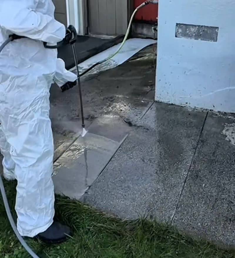 Pressure washer cutting a clean strip through dark grime on an exposed-aggregate concrete walkway